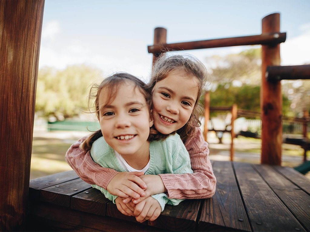 minimally-invasive-dentistry-healthy-smiles Smiling twin girls at a playground, representing healthy smiles with minimally invasive dentistry.